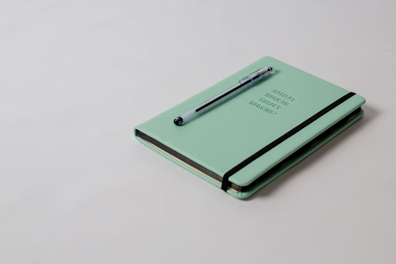 A mint green notebook with a pen on a plain background