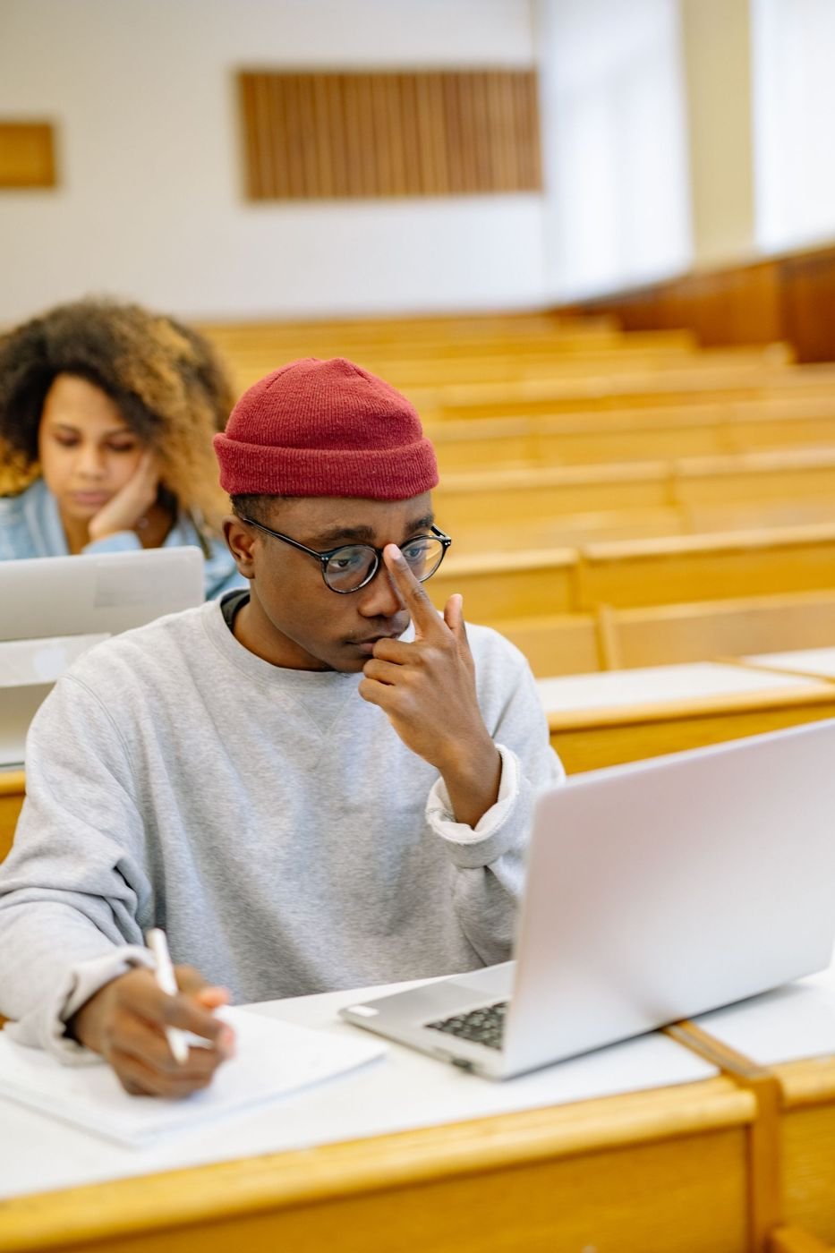 A student taking notes beside a laptop in a lecture hall