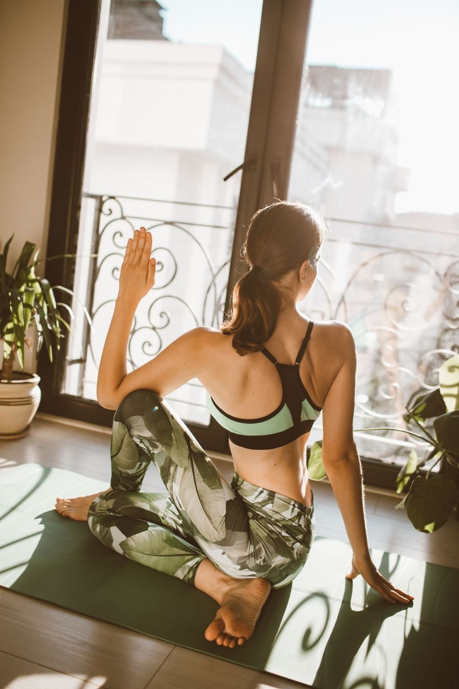 A woman stretching on a yoga mat beside a window