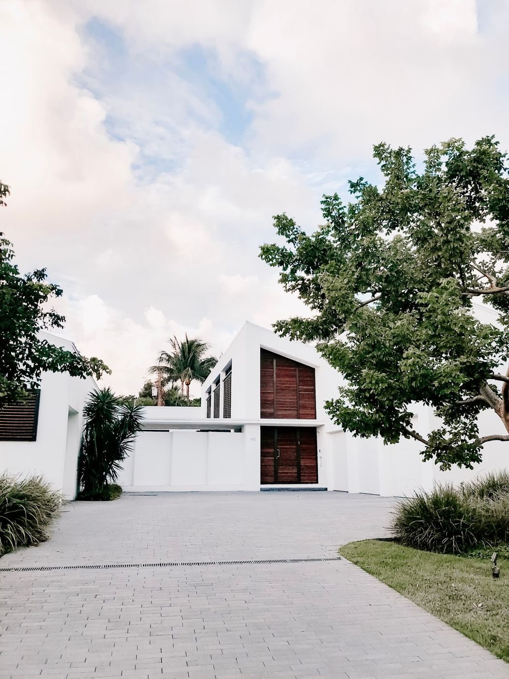 A modern white house with a paved driveway and trees