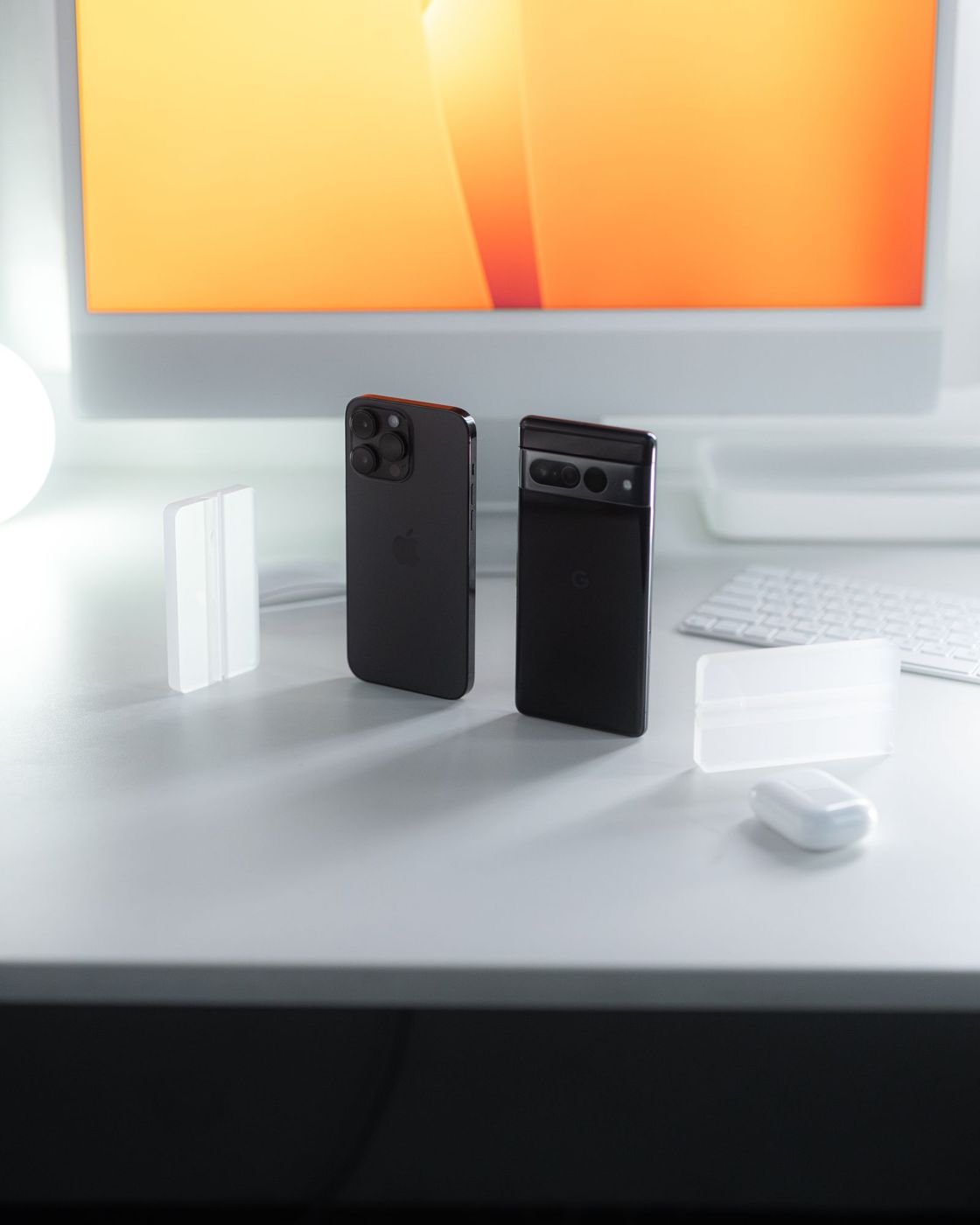 Two smartphones beside a monitor on a clean white desk