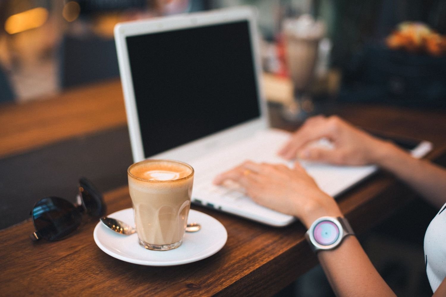 A person typing on a laptop beside a latte on a wooden table