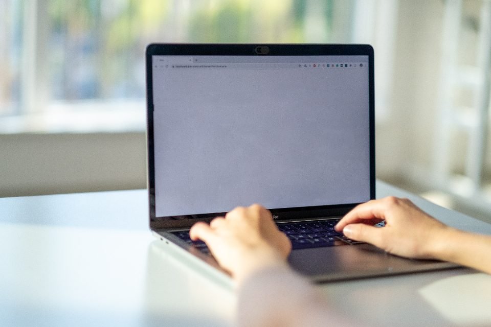 Hands typing on a laptop by a bright window